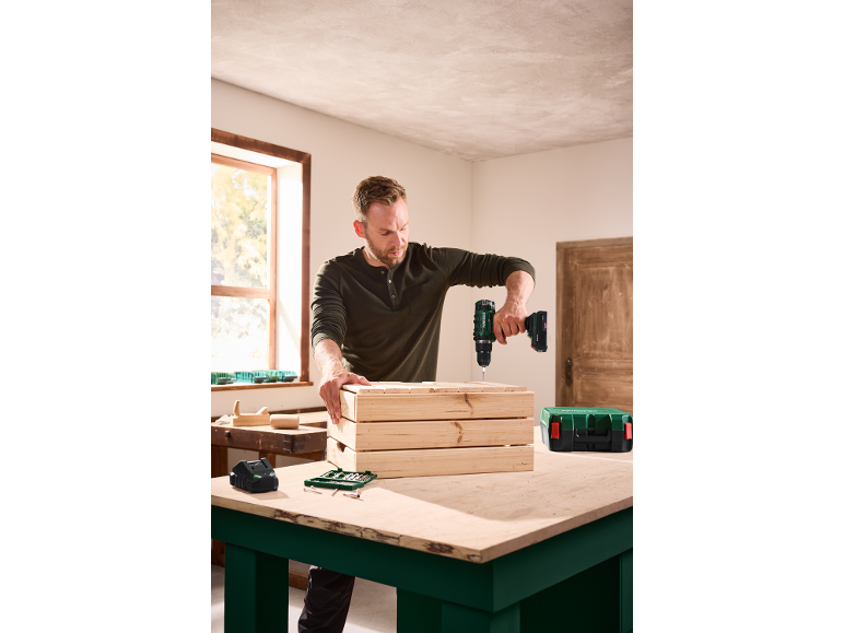 Man drilling into a wooden crate with a cordless drill on a workbench.