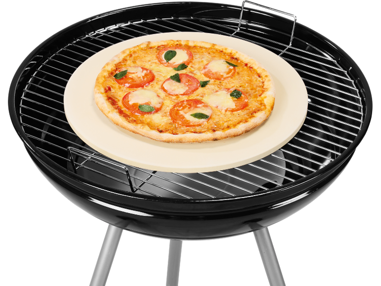 Margherita pizza on a round pizza stone on a black barbecue grill.