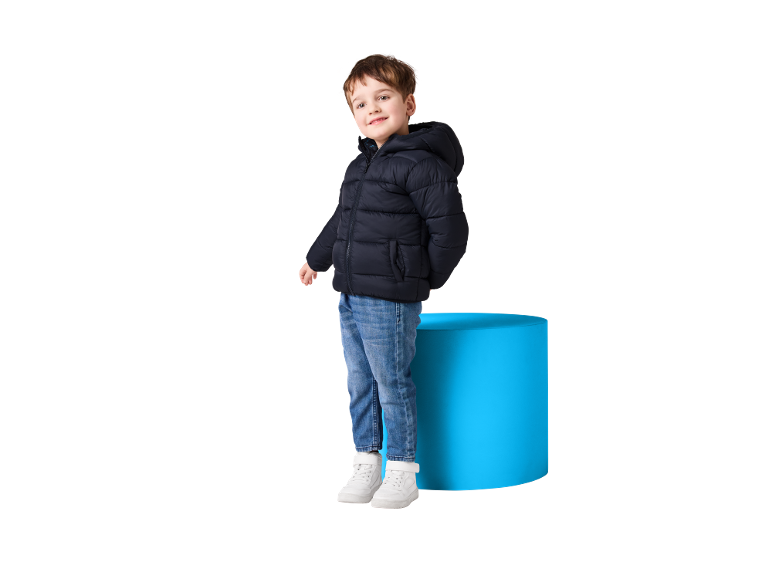Smiling boy in dark blue puffer jacket, jeans, and white sneakers.