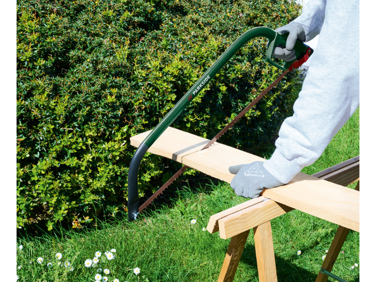 Man cutting a wooden board with a saw on a wooden sawhorse in the garden.