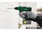 Gloved person drilling into a white brick wall with a cordless drill.