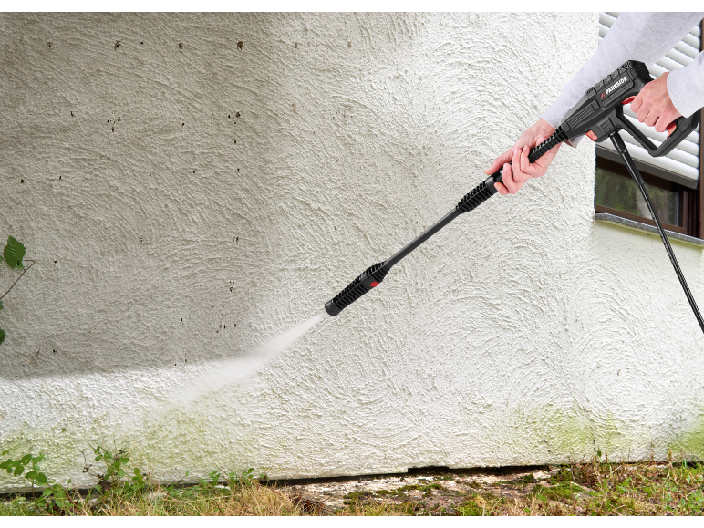 Person cleaning a dirty wall with a pressure washer, removing green algae.