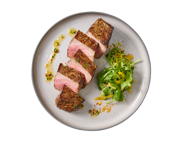Sliced beef steak with sauce and salad on a plate.