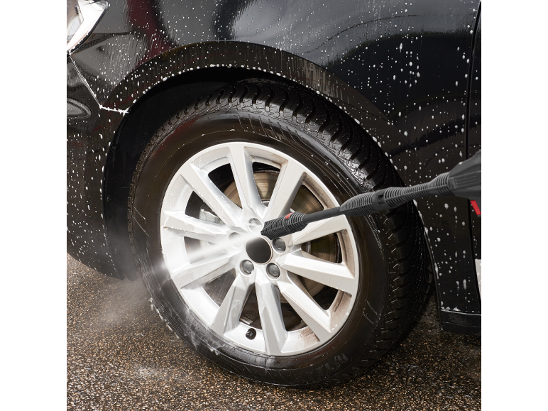 Washing black car with pressure washer, with foam and splashing water.