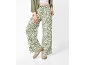 Women's wide-leg trousers with green and white floral print, paired with a green shirt and beige sneakers.