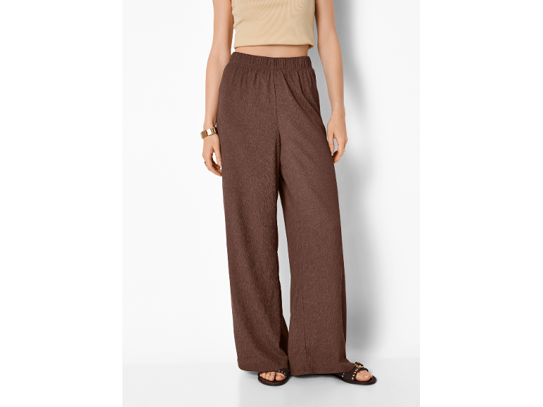 Woman in brown wide-leg trousers and a beige crop top, with sandals and a gold bracelet.