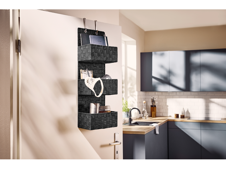Black over-the-door organizer with three compartments, hanging on a kitchen door.