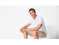 Man in white polo shirt and beige shorts sitting on a white chair.
