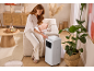 Woman adjusting a portable air conditioner in a living room with natural tones.