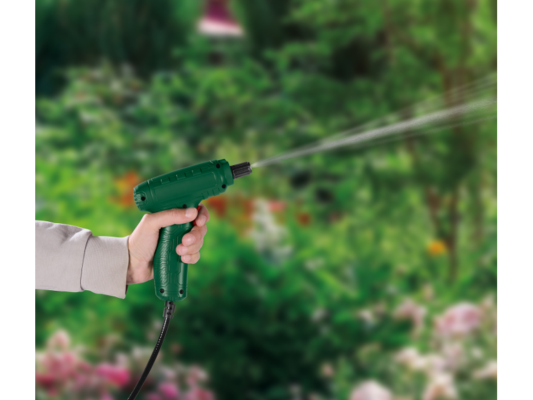 Hand holding a green garden sprayer, watering plants in a blurred garden background.