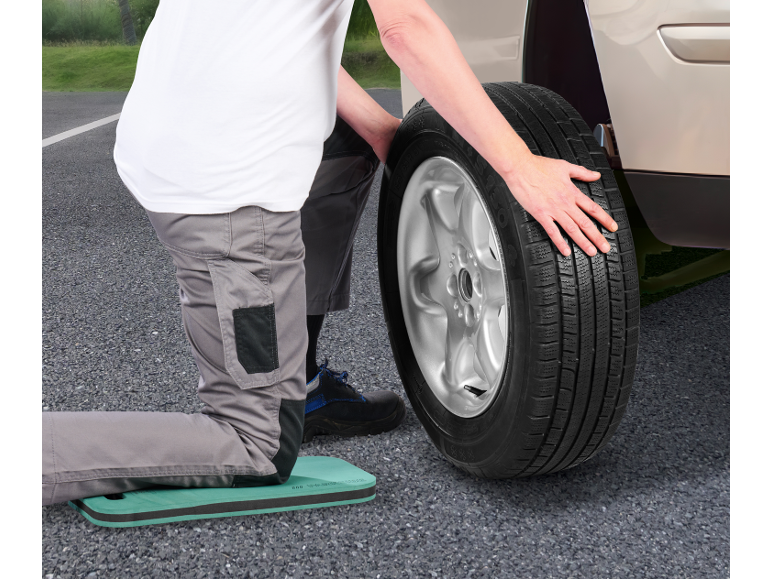 Man changing a car tire, kneeling on a kneeling pad.
