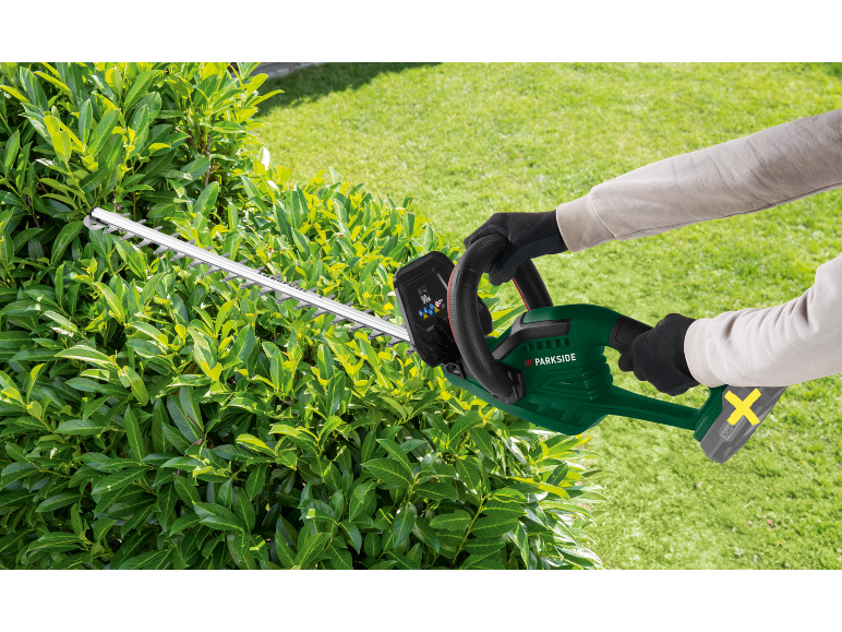 Gloved person trimming a hedge with a cordless hedge trimmer.