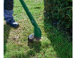 Person trimming grass with a green electric grass trimmer next to a hedge.