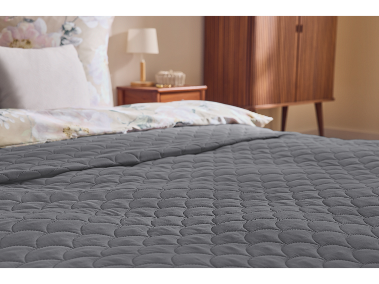 Bed with grey quilted duvet and floral pattern pillows in a cozy bedroom.