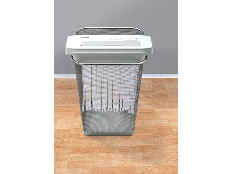 White paper shredder in a mesh waste bin on a wooden floor.