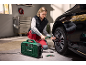 A woman inflates a car tire with a portable compressor in a garage.
