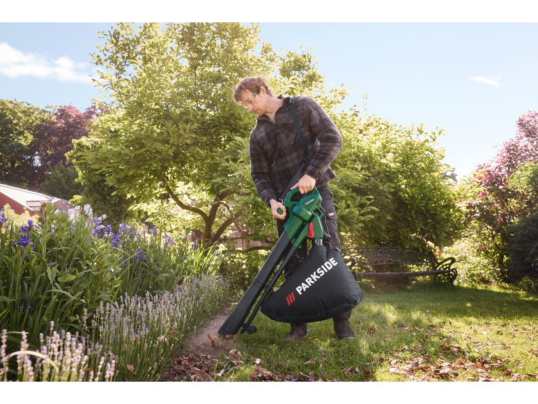 Man uses an electric leaf vacuum in a garden.