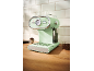 Mint green espresso machine with a pressure gauge, cups, and coffee beans on a wooden counter.