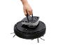 Hand holding a water tank from a black robotic vacuum cleaner.