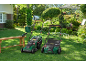Two lawnmowers and a hedge trimmer on a wooden bench in a sunny garden.