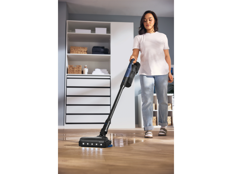 Woman cleaning a wooden floor with a cordless vacuum cleaner with mop function.