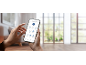 Hands holding a smartphone with a robot vacuum cleaner control app in a living room.