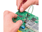 Hands connecting cables to a green circuit board with electronic components.
