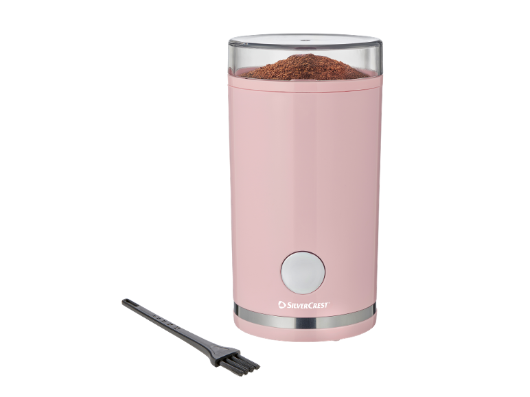 Pink coffee grinder with ground coffee and a cleaning brush.