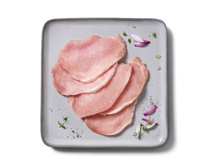 Raw pork cutlets with red onion, pepper, and herbs on a grey plate.