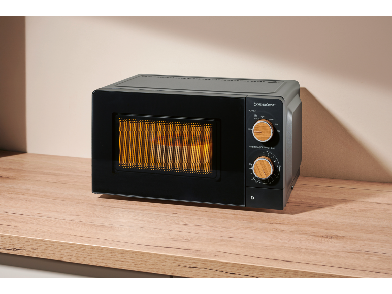 Black microwave with wooden details on a wooden countertop, with food inside.