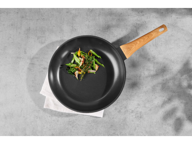Frying pan with wooden handle and cooked vegetables on a concrete background.