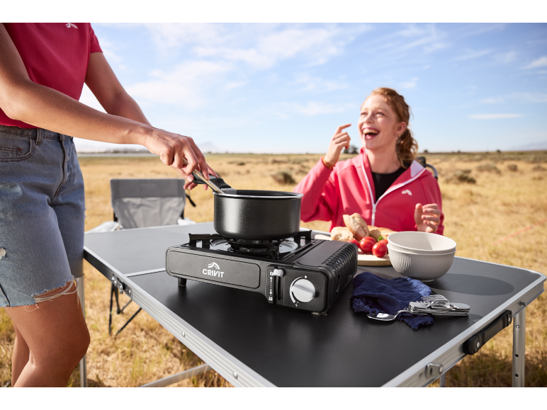 Woman cooking on a portable gas stove on a folding table while camping.