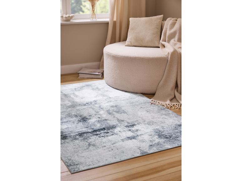 Rug with abstract grey pattern, beige pouf and throw in a living room.