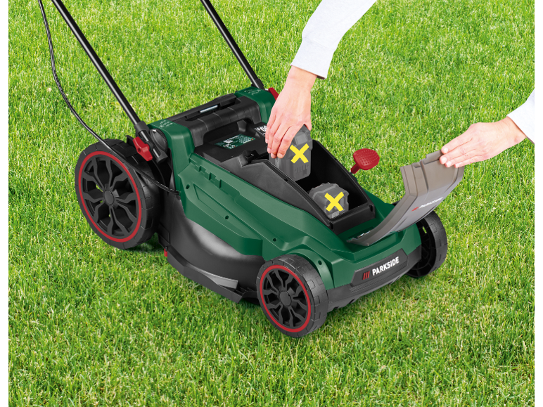 Cordless lawnmower with two batteries being inserted on a green lawn