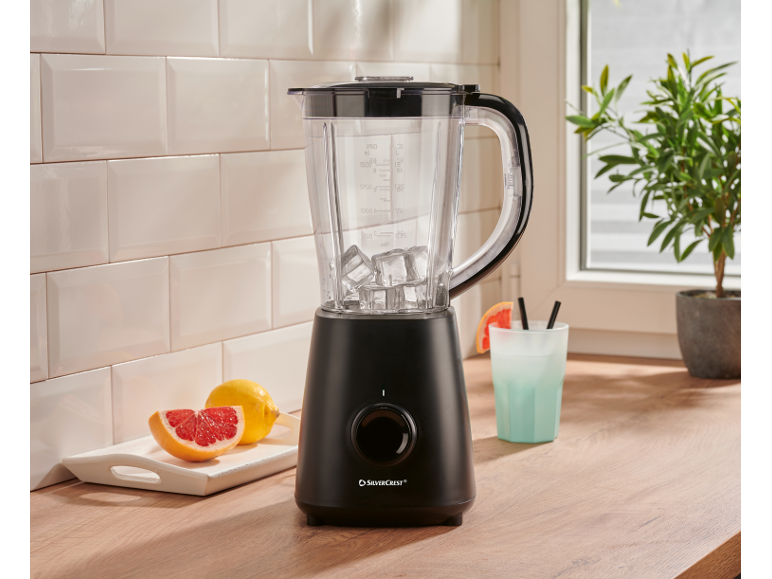 Black jug blender with ice cubes, citrus fruits, and a refreshing drink in a bright kitchen.