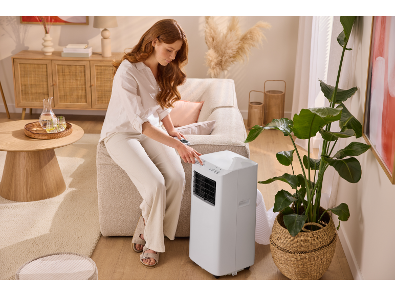 Woman adjusting a portable air conditioner in a living room with natural tones.