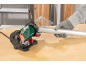 Worker grinds a metal pipe with a bench grinder, wearing protective gloves.