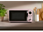Pink microwave on a kitchen counter with a plant and wooden utensils.