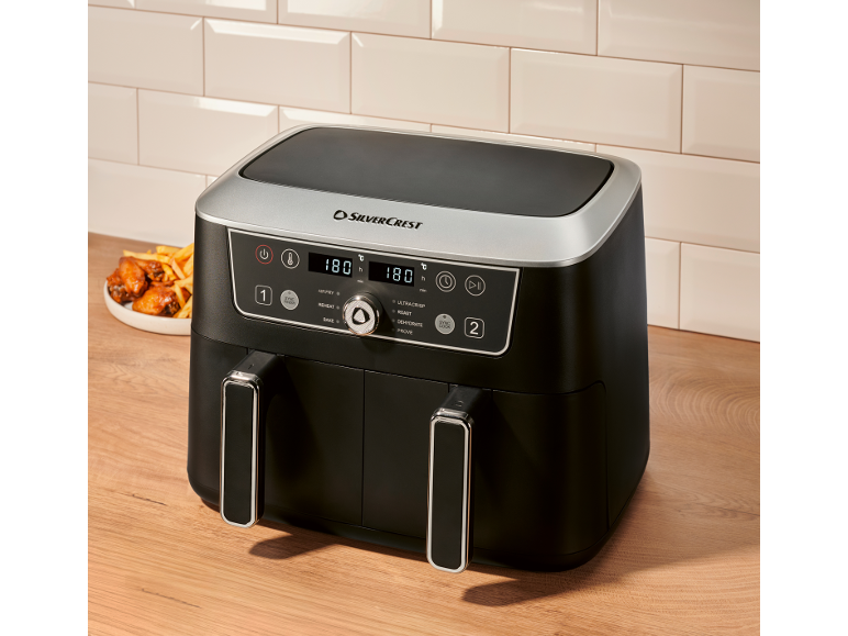 Black dual-drawer air fryer with digital display, chicken wings, and fries.
