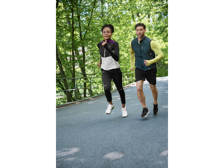Two runners in sportswear jogging outdoors, woman in a jacket and man in a vest.
