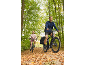 Man and woman cycling on a forest path covered with autumn leaves.