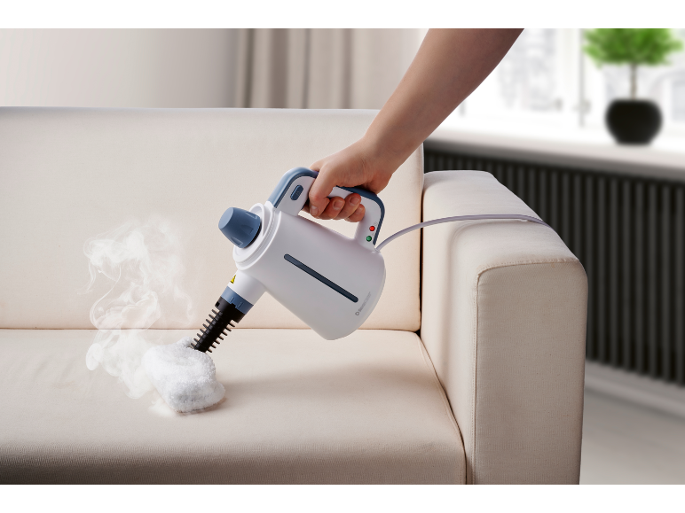 Handheld steam cleaner cleaning a cream sofa, with steam visible.