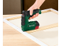 Green and black electric stapler stapling a canvas onto a wooden frame.