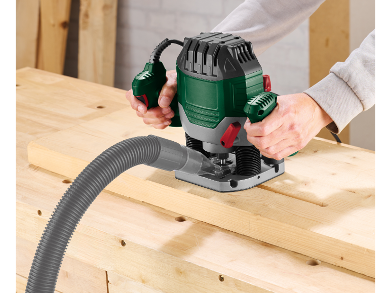 Man using a wood router with a vacuum cleaner attachment on a workbench.