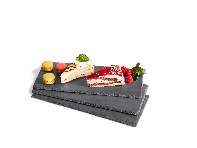 Cake slices and macarons on slate platters, garnished with raspberries and mint.