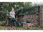 Woman with a leaf blower and a chainsaw in front of a firewood storage.