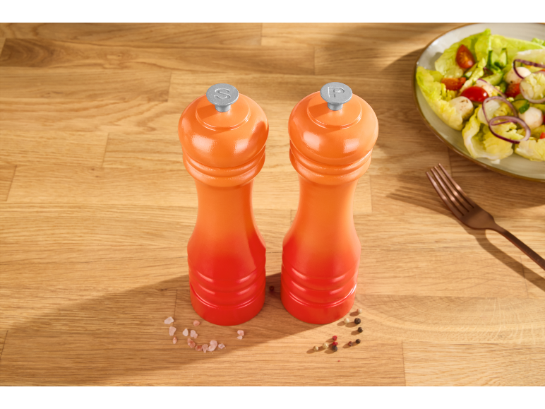 Orange salt and pepper grinders on a wooden table with a salad.