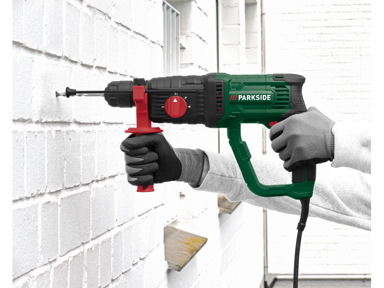 Man drilling a hole into a white brick wall with a rotary hammer.