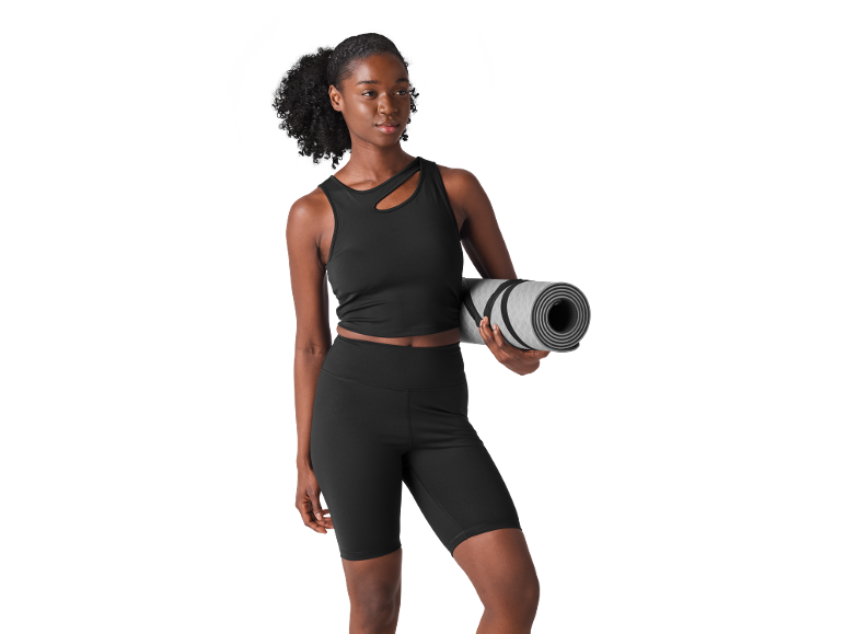 Woman in black sports top and shorts holding a rolled yoga mat.