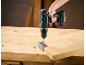 Cordless drill driving a screw into a metal bracket attached to a wooden board on a workbench.